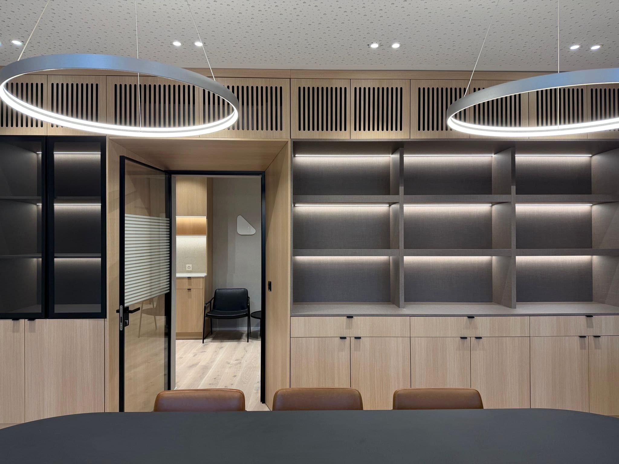 Büro: Sitzungszimmer mit Regalwand aus Eiche, beleuchteten Fächern und Glastüre zur Teeküche